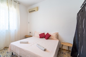 Une chambre à coucher avec un lit, des oreillers, une table de chevet, un climatiseur et un sol à motifs.