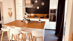 A modern kitchen with a wooden island, white bar stools, a built-in oven, and a black backsplash. - Quiet villa in charming Provence village (Mouriès)