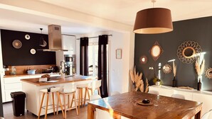 A modern kitchen with a central island, white chairs, and a dining table with a wooden top. - Quiet villa in charming Provence village (Mouriès)
