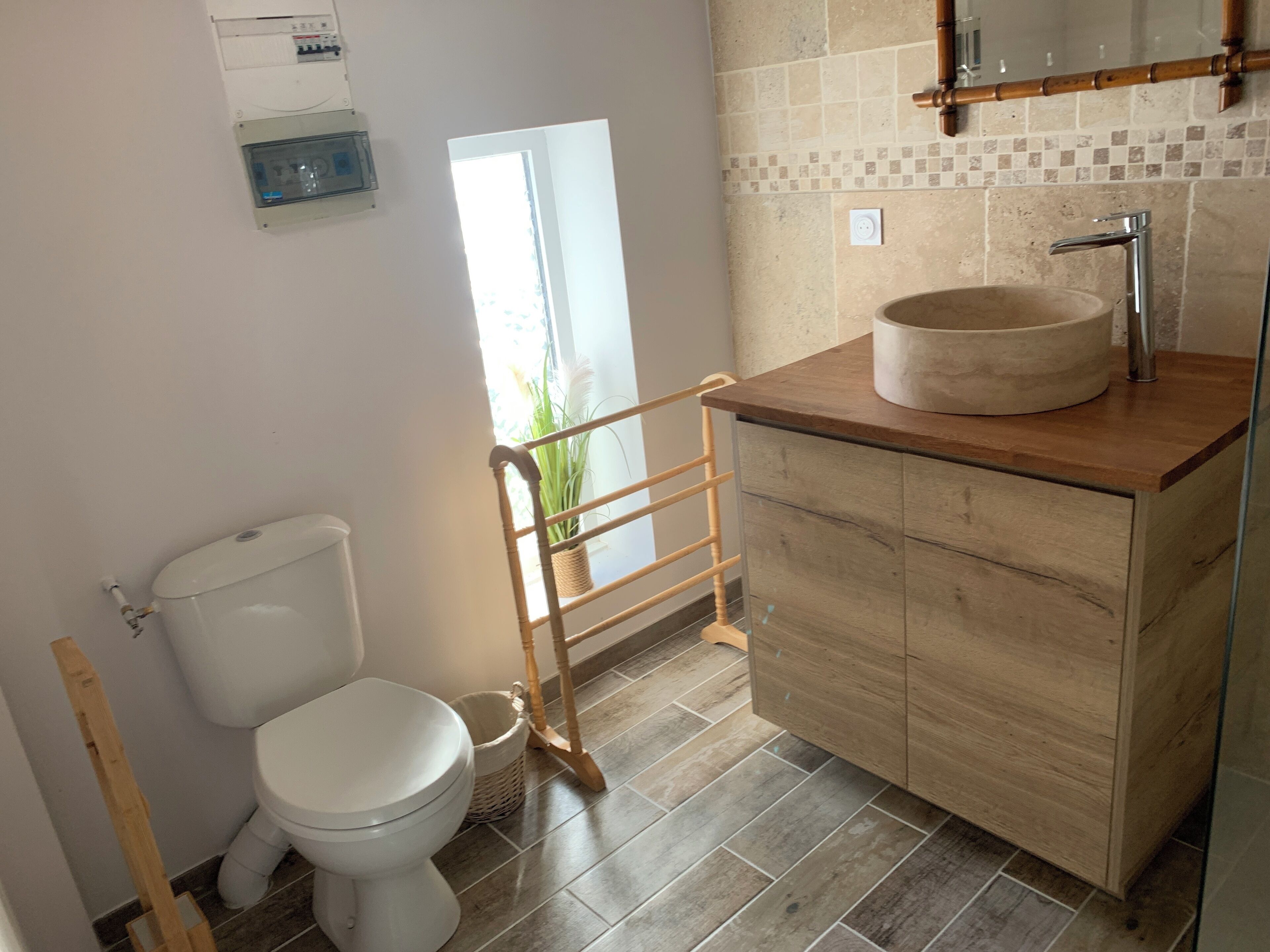Un bagno con il water, un mobiletto in legno con lavabo, uno specchio e una finestra.