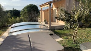A modern outdoor pool area with a pergola, surrounded by greenery and a building with a beige facade. - Bed and breakfast at Gandja (Bédoin)