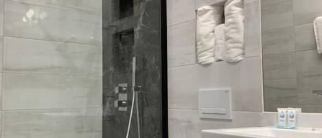 Un baño moderno con ducha de vidrio, inodoro blanco y tocador con espejo y toallero.