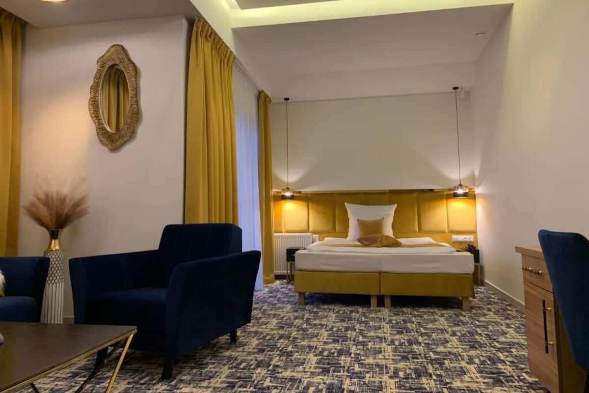 Ein Hotelzimmer mit einem großen Bett, zwei Sesseln, einem kleinen Tisch und einem Nachttisch.