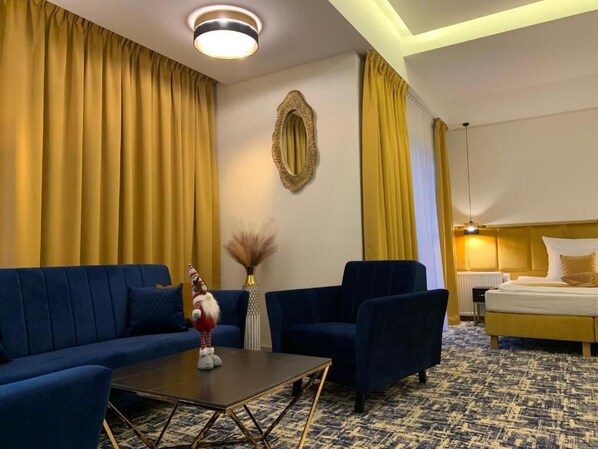 A hotel room with a blue sofa, two armchairs, a small table, and a bed with a yellow headboard. - Centrum Piramida (Boleslawiec)