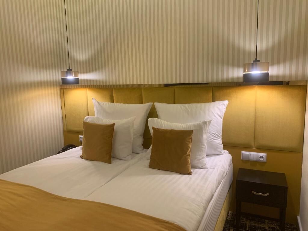 A hotel room with a large bed, two bedside lamps, a nightstand, and a wall-mounted control panel.