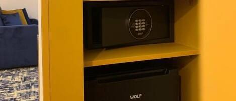 A compact kitchen area with a microwave, kettle, and coffee maker on a yellow shelf, and a black refrigerator below.
