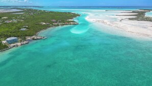 An aerial view of a coastal area with clear turquoise waters, a small settlement with houses, and a dock. - Panoramic Ocean Views, Private Beach, Dock, Pickleball, and Housekeeping (Rolletown)