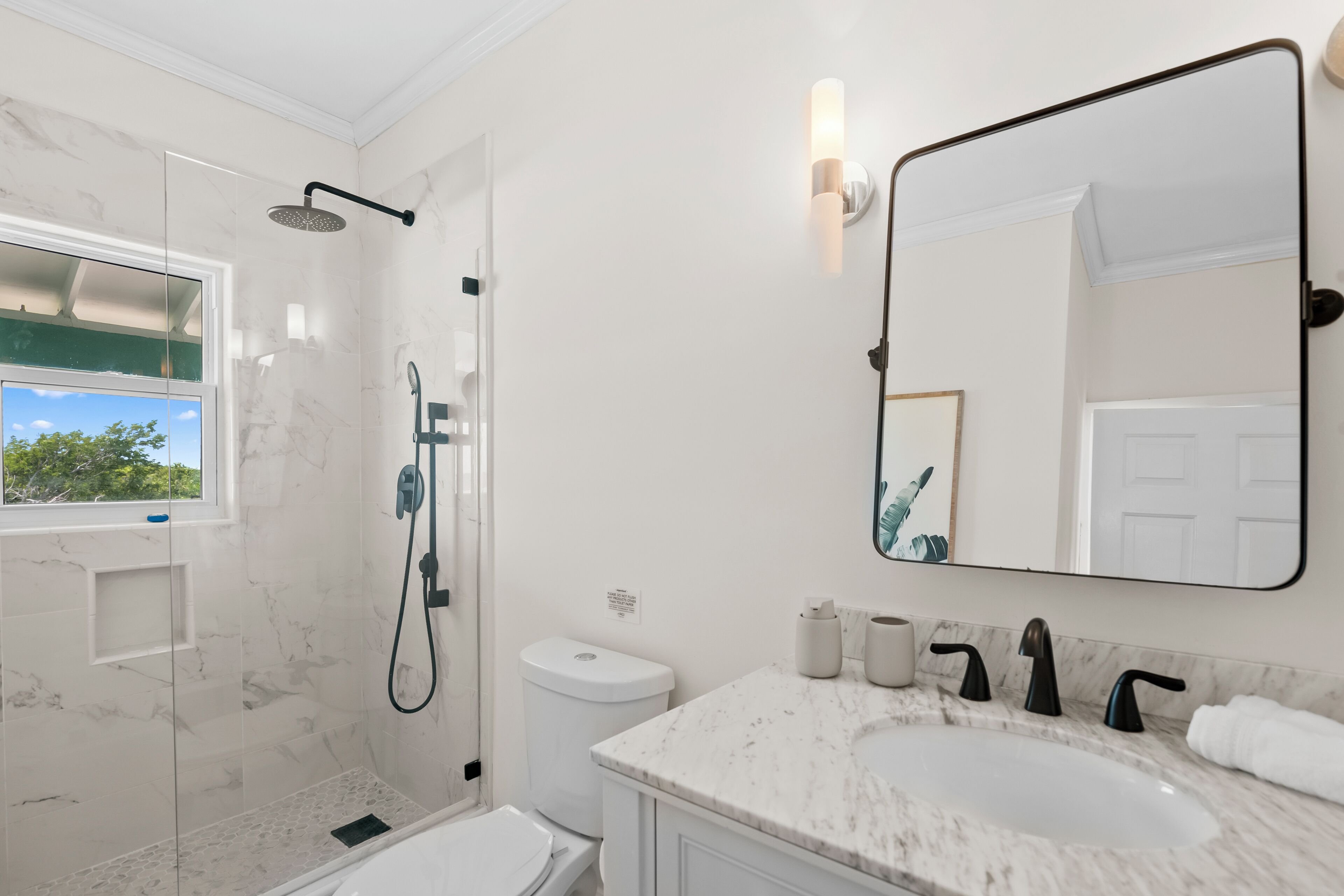 A modern bathroom with a glass-enclosed shower, a large mirror, and a marble countertop.