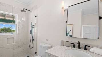 A modern bathroom with a glass-enclosed shower, a large mirror, and a marble countertop.