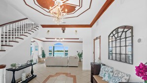 A spacious living area with a staircase, a large window, and a view of the outdoors. - Panoramic Ocean Views, Private Beach, Dock, Pickleball, and Housekeeping (Rolletown)