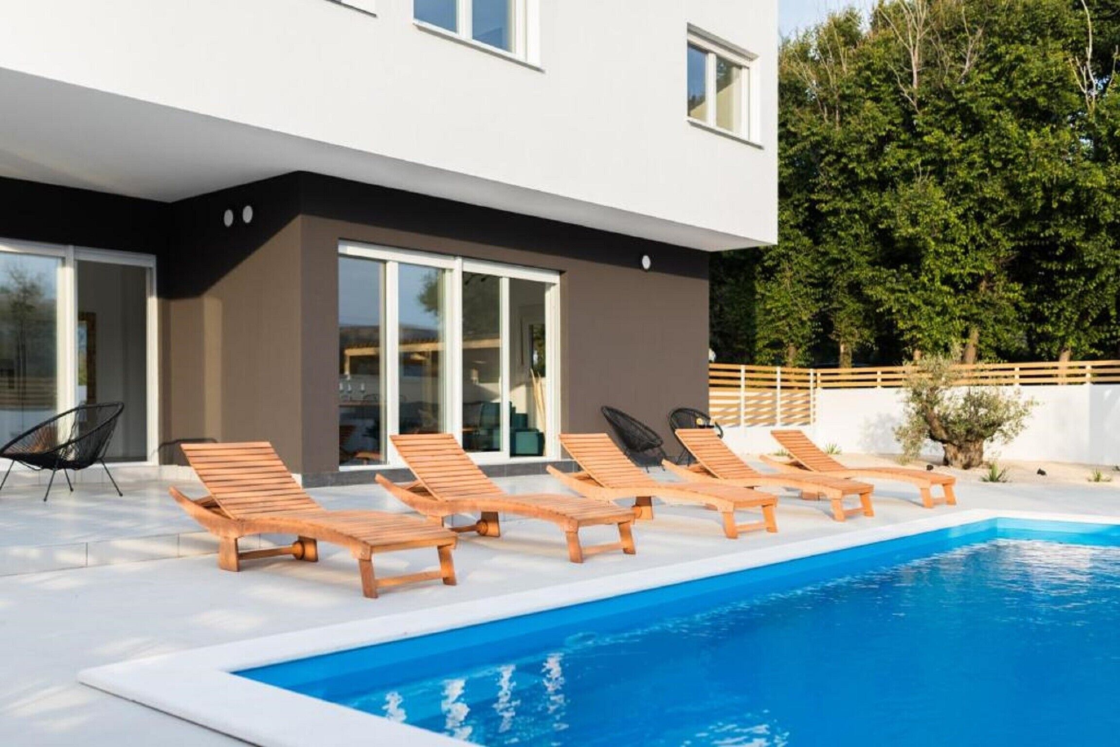 A modern outdoor pool area with wooden loungers and a clear blue pool.