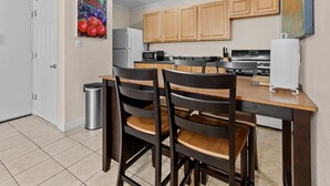 A compact kitchen with wooden cabinets, a microwave, a refrigerator, and a dining table with chairs.