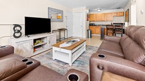 A modern living room with a flat-screen TV, leather sofas, a coffee table, and a kitchen in the background.