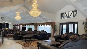 A spacious living room with a large L-shaped sofa set, a coffee table, and a chandelier. There is a large window with curtains and a view of the outdoors. - Spacious 6000 sf 6-bedroom villa in lovely Fremont with private gate, and view (Fremont)