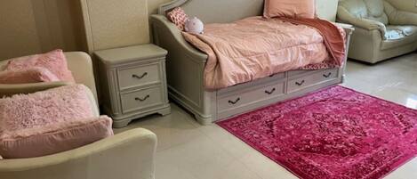 Quarto com cama, mesas de cabeceira, uma cadeira e um tapete vermelho.