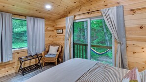 Een houten kamer met een bed, een stoel, een klein tafeltje en een hangmat.