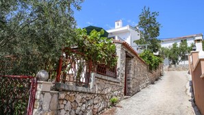 Un estrecho sendero de piedra que conduce a un edificio blanco con una puerta roja y una pérgola cubierta de enredaderas.