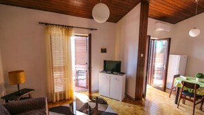 Una sala de estar acogedora con un sofá, una mesa de centro de vidrio y un televisor sobre un mueble. Se observa un comedor con mesa y sillas, y una cocina visible a través de un umbral abierto.