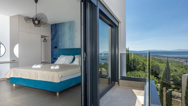 A modern bedroom with a large bed, a view of the city, and a balcony.