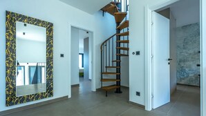 A spacious hallway with a marble-patterned wall, a wooden spiral staircase, and a large mirror.