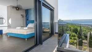 A modern bedroom with a bed, a large sliding glass door leading to a balcony with a city view.