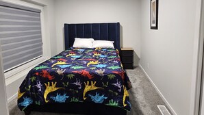 A bedroom with a bed, a headboard, a bedside table, a window with blinds, and a picture on the wall. - Modern 1-Bedroom Garden Suite | Above Ground Suite | Side Parking | Chappelle (Edmonton)