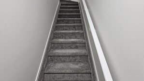 A narrow staircase with a handrail, carpeted steps, and white walls. - Modern 1-Bedroom Garden Suite | Above Ground Suite | Side Parking | Chappelle (Edmonton)