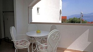 Un balcon avec une table blanche et quatre chaises, une vue sur la mer et un bâtiment en arrière-plan.