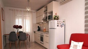 Un espace de vie compact comprenant un coin cuisine, un coin repas avec deux chaises, un canapé rouge et un lustre.