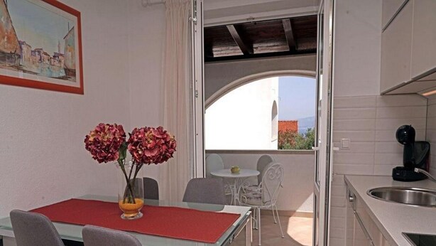 Un coin repas avec une table et des chaises, un vase rempli de fleurs et une vue sur un bâtiment par une porte ouverte.