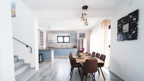 Eine moderne Küche mit einer zentralen Kochinsel, einem Essbereich mit Holztisch und -stühlen sowie einer Treppe, die in ein weiteres Geschoss führt.