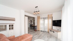 Ein modernes Wohnzimmer mit einer Couch, einem runden Couchtisch, einem Fernseher und einer Küche im Hintergrund.