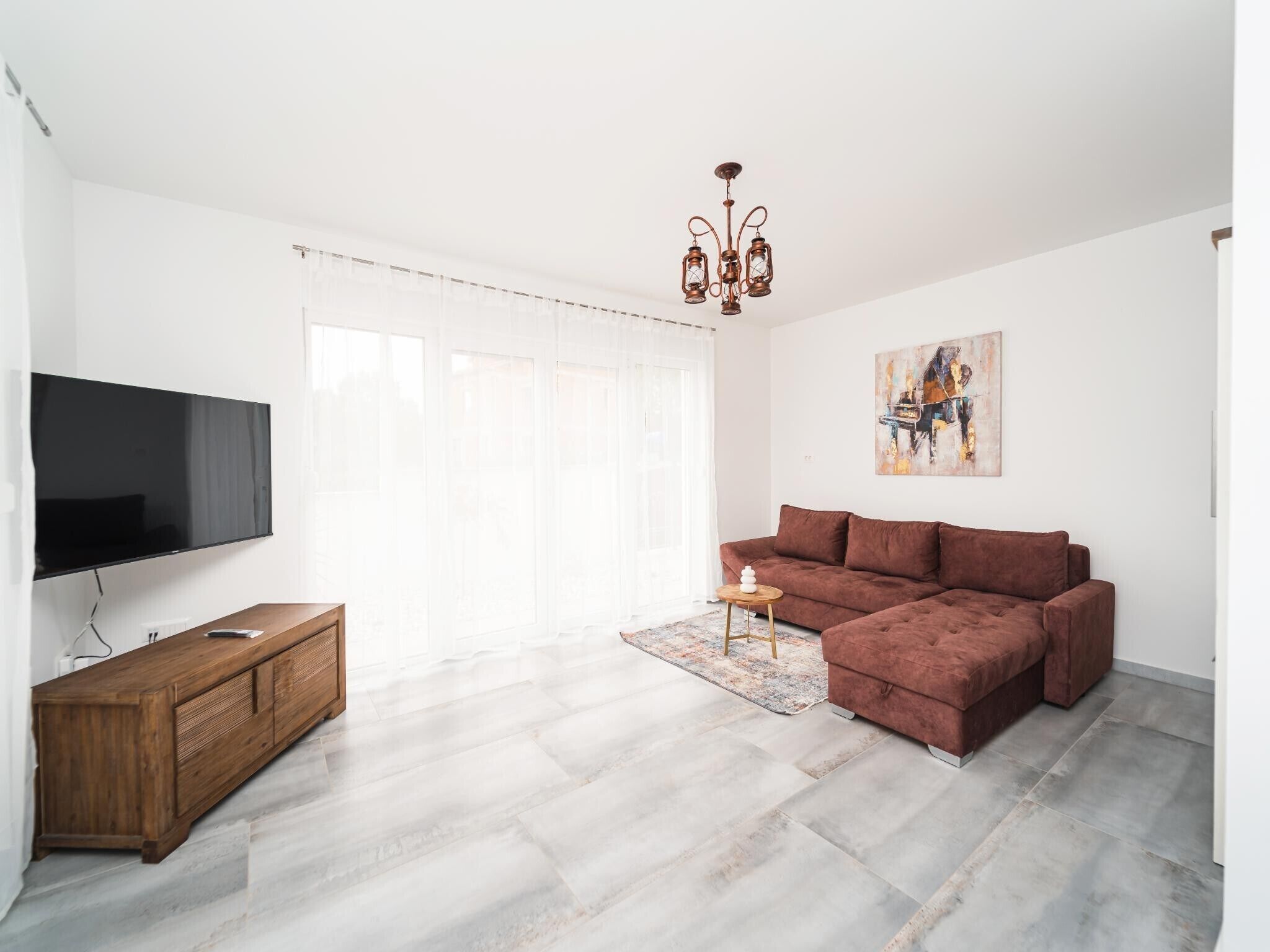 Un salon moderne avec un canapé d’angle, un téléviseur à écran plat, un meuble en bois et un lustre.