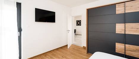 A modern bedroom with a wooden floor, a large wardrobe with a black and wood panel design, and a flat-screen TV mounted on the wall.