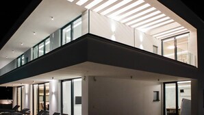 A modern interior with a sloped ceiling, glass railings, and a balcony with seating. - Sunset Serenity Villa with Pool, Gym and Sauna - Six Bedroom Villa with Pool (Kastel Kambelovac)