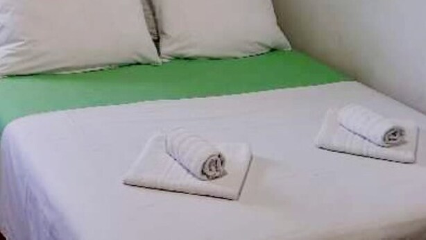 Una cama con ropa blanca, almohadas, un cabecero verde y dos toallas enrolladas sobre la cama.