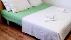 Una cama individual con un colchón verde y ropa de cama blanca, dos almohadas y dos toallas enrolladas sobre la cama.