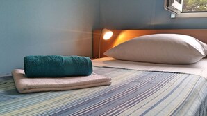 Una cama bien hecha con ropa de cama a rayas, una toalla azul turquesa y una almohada color beige.