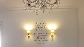 Une chambre à coucher avec un lustre, deux lampes fixées au mur, un lit recouvert d’une couverture verte et une citation affichée sur le mur.