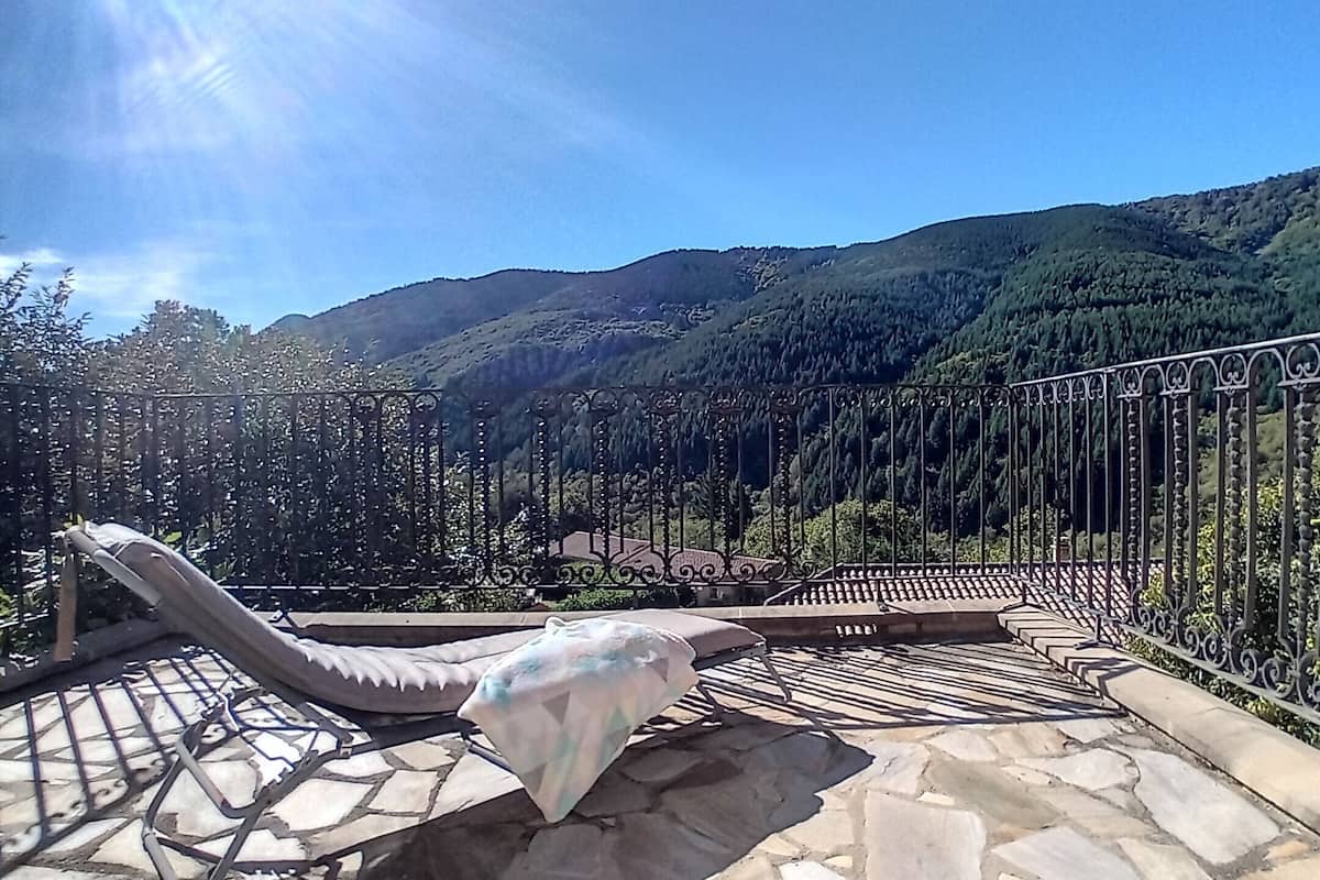 A stone patio with a metal railing overlooking a mountainous landscape.