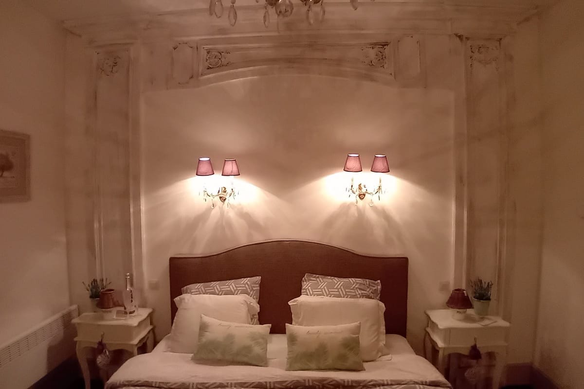A bedroom with a large bed, two bedside tables, and wall-mounted lamps.