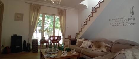 A living room with a sofa, a coffee table, a chandelier, a staircase, and a window with curtains.