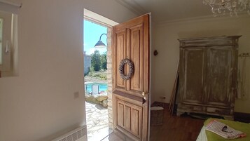 Um quarto com porta de madeira, uma cesta de vime, uma mesa verde e um guarda-roupa antigo.