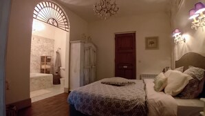 A bedroom with a patterned bedspread, a wooden door, a chandelier, and a wall-mounted light fixture. - Villa Montagnes (Valgorge)