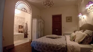 Quarto com colcha estampada, porta de madeira, lustre e luminária fixada na parede.