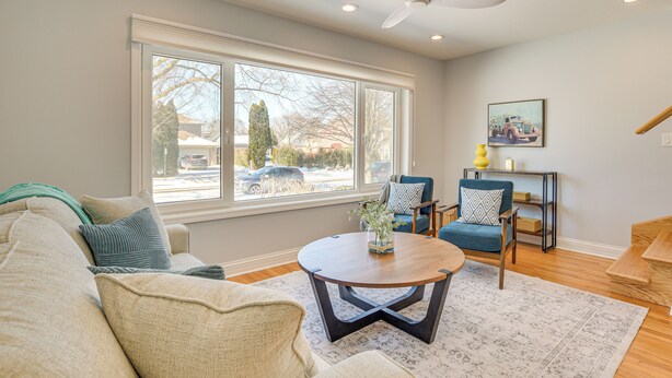 A living room with a large window, a ceiling fan, a round coffee table, and a blue armchair. - 2 Mi to Northwestern: Updated Home w/ Game Room! (Evanston)