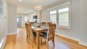 A dining area with a wooden table and chairs, a chandelier, and a view of the outside through a large window. - 2 Mi to Northwestern: Updated Home w/ Game Room! (Evanston)