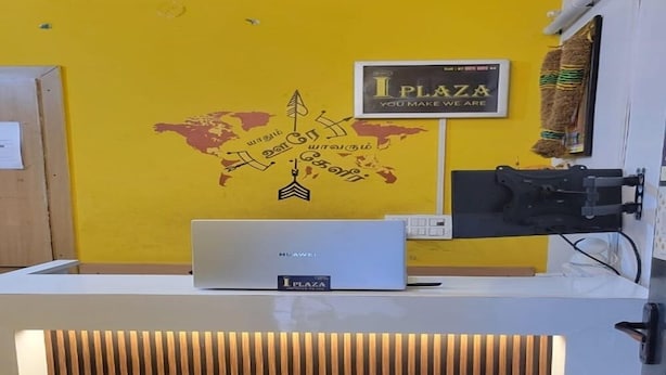 A reception desk with a Huawei device, a world map mural, and a sign reading "I PLAZA YOU MAKE WE ARE". - HOTEL I PLAZA (Madurai)