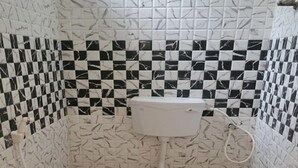 A small bathroom with a toilet, a shower, and a sink. The walls are tiled with a marble pattern. - HOTEL I PLAZA (Madurai)