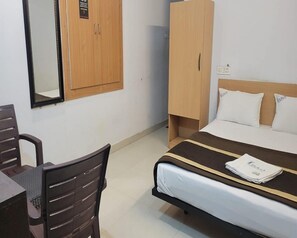 A hotel room with a bed, a desk, a chair, a wardrobe, and a mirror. - HOTEL I PLAZA (Madurai)